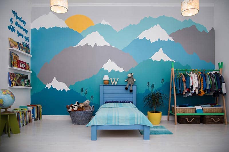 A spacious boy bedroom with a beautiful turquoise and grey mountain wall mural and bookshelves